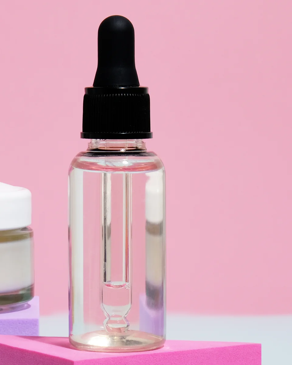 A clear dropper bottle of oil on a pink block