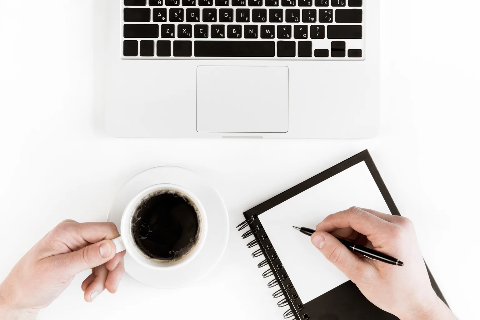Cannabis content writing starts with a plan: a hand writes notes in a notebook next to a laptop and a cup of coffee